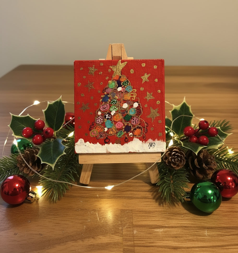 Small painting of a Christmas tree on a red background with a wooden easel.