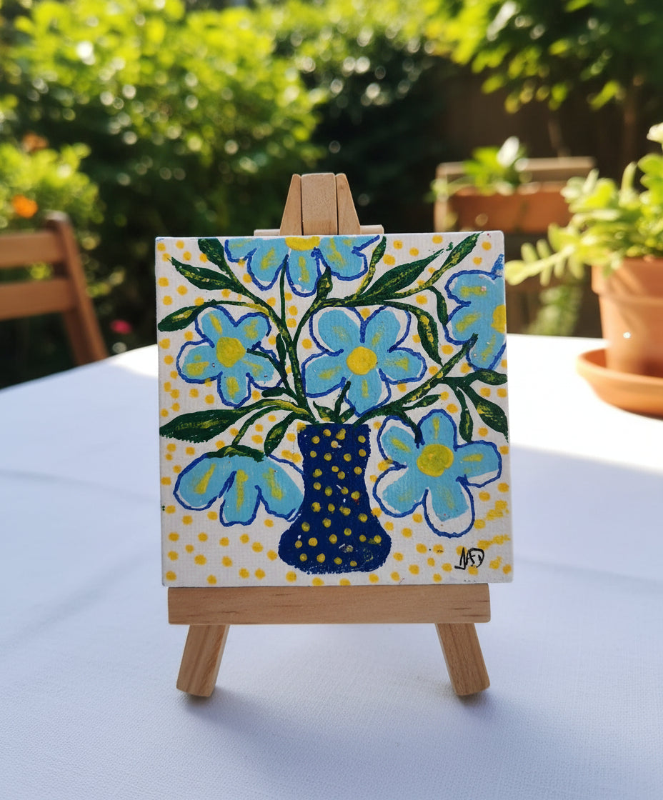 Small painting of blue flowers in a polka dot vase on a white background